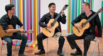 Ian O’Sullivan (left) with two of his students, playing music in front of MFA student Tom Walker's paintings at the Art Gallery. 