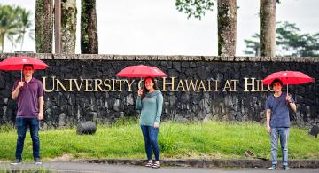 students with umbrellas in front of UH Hilo sign